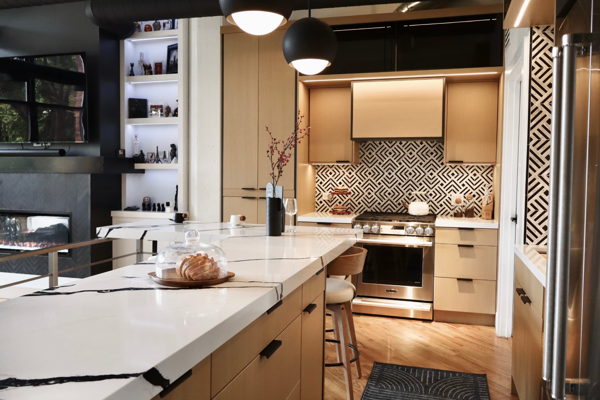 Loft kitchen with natural white oak flat-panel cabinetry, a marble-look quartz island and matte black pendant lighting