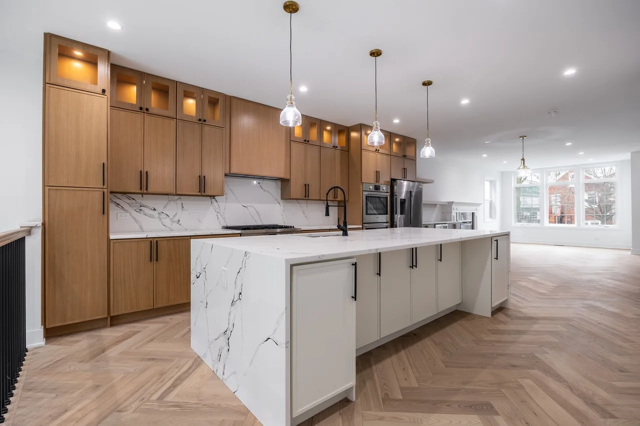 Walnut cabinetry kitchen with a marble waterfall island, pendant lighting and herringbone wood flooring