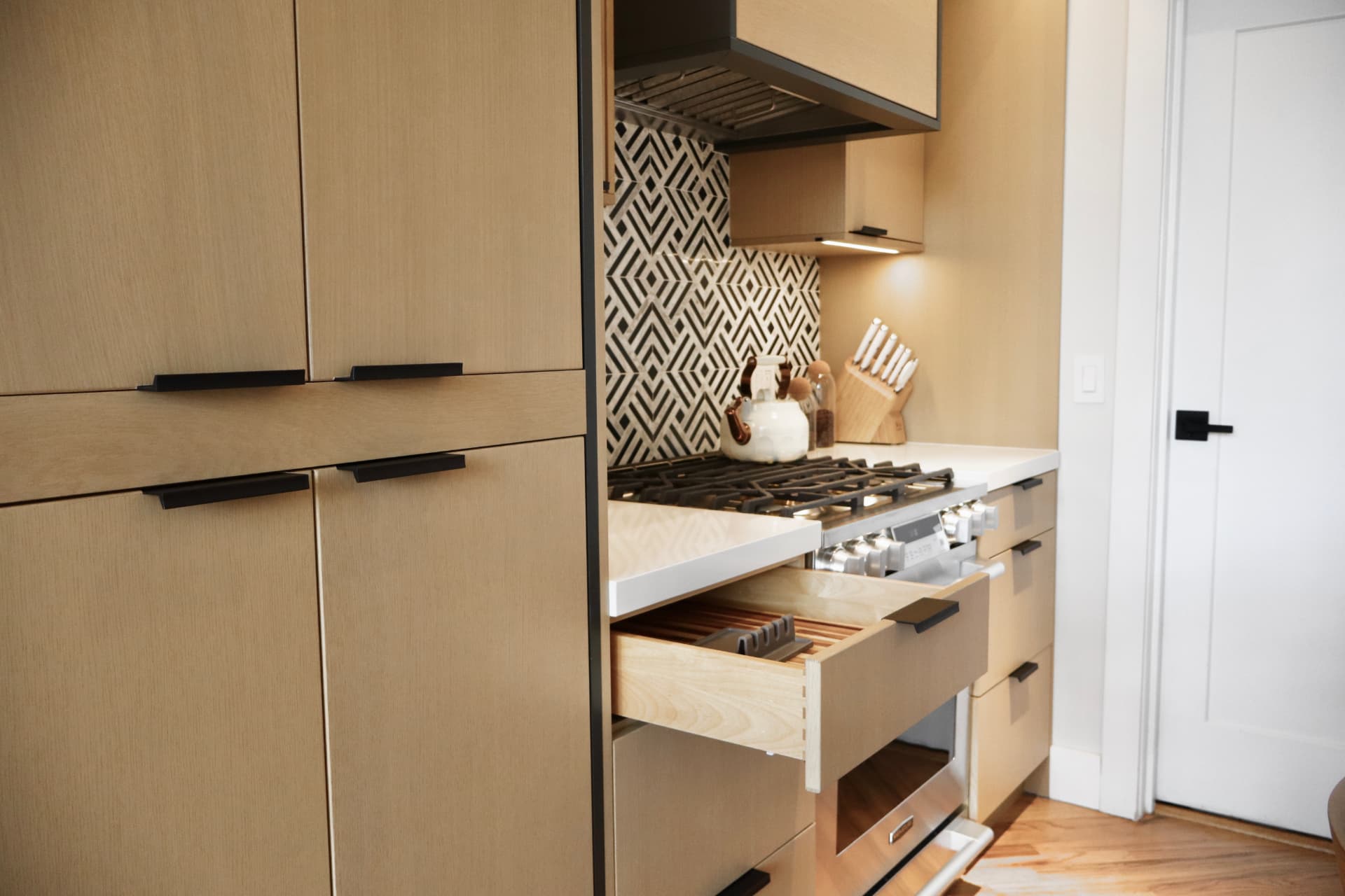 Rift-cut white oak cabinetry with matte black pulls, an open drawer and a geometric black and white backsplash